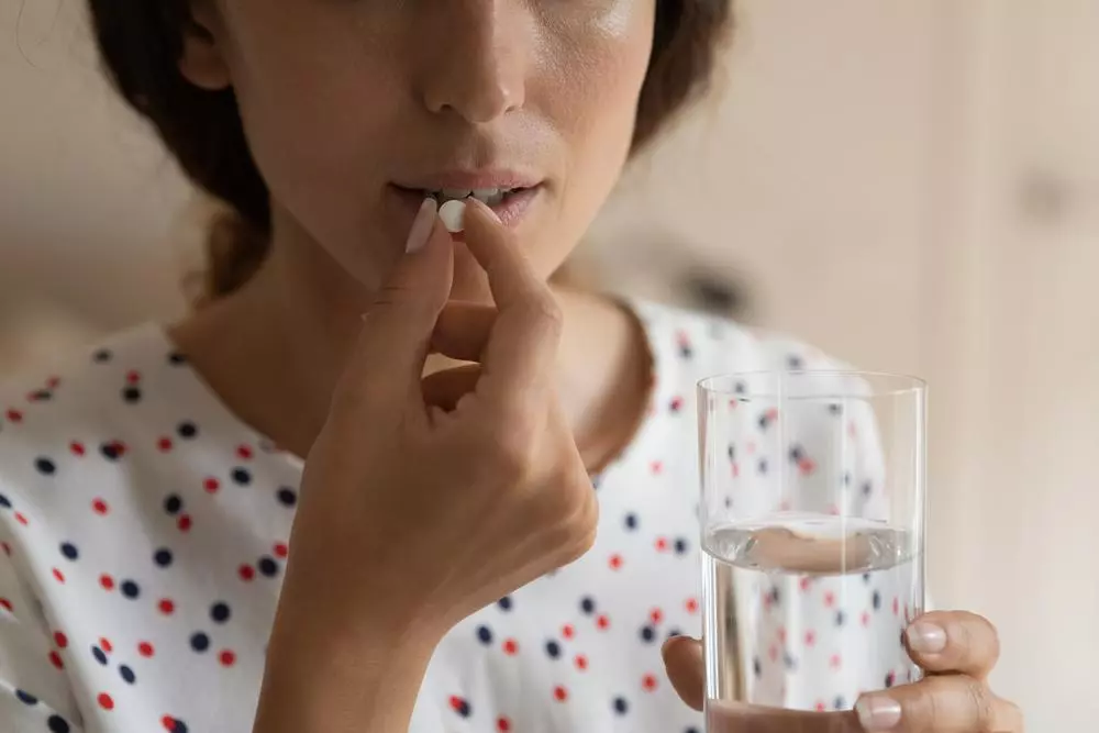 Young lady holds a glass of water and prepares to swallow a pill