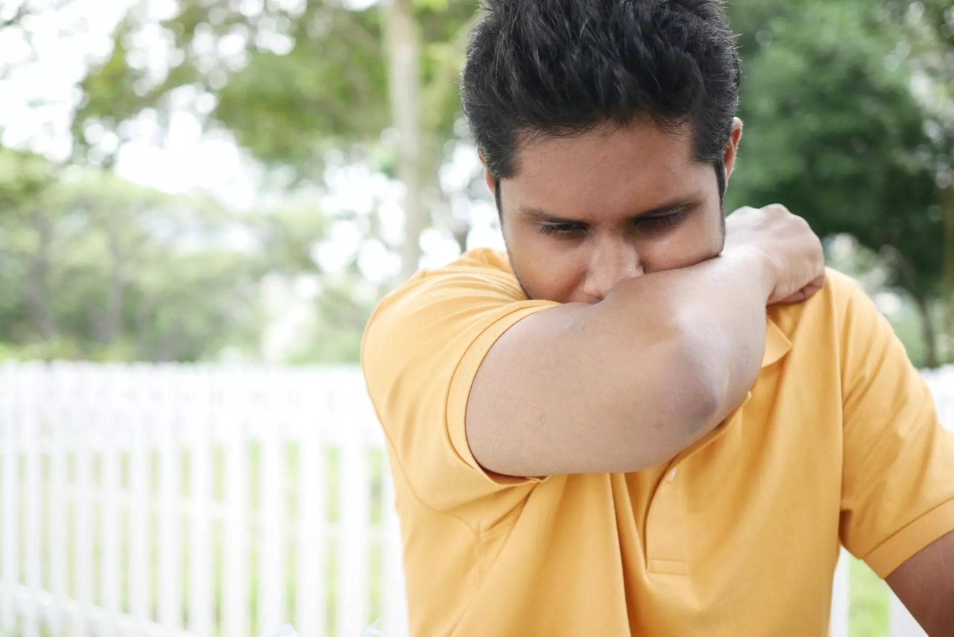 Young man using his arm to cover his nose and mouth.