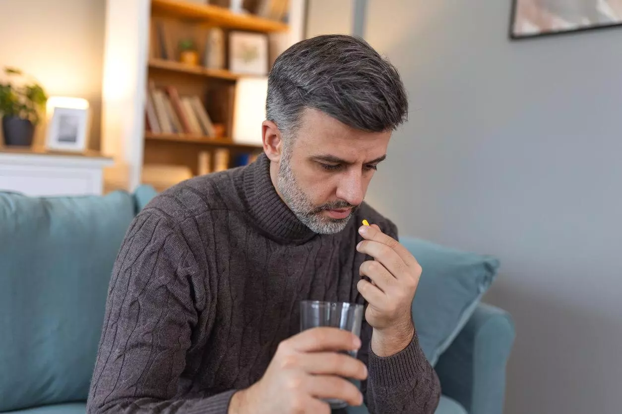 Man taking a pill and drinking a glass of water.