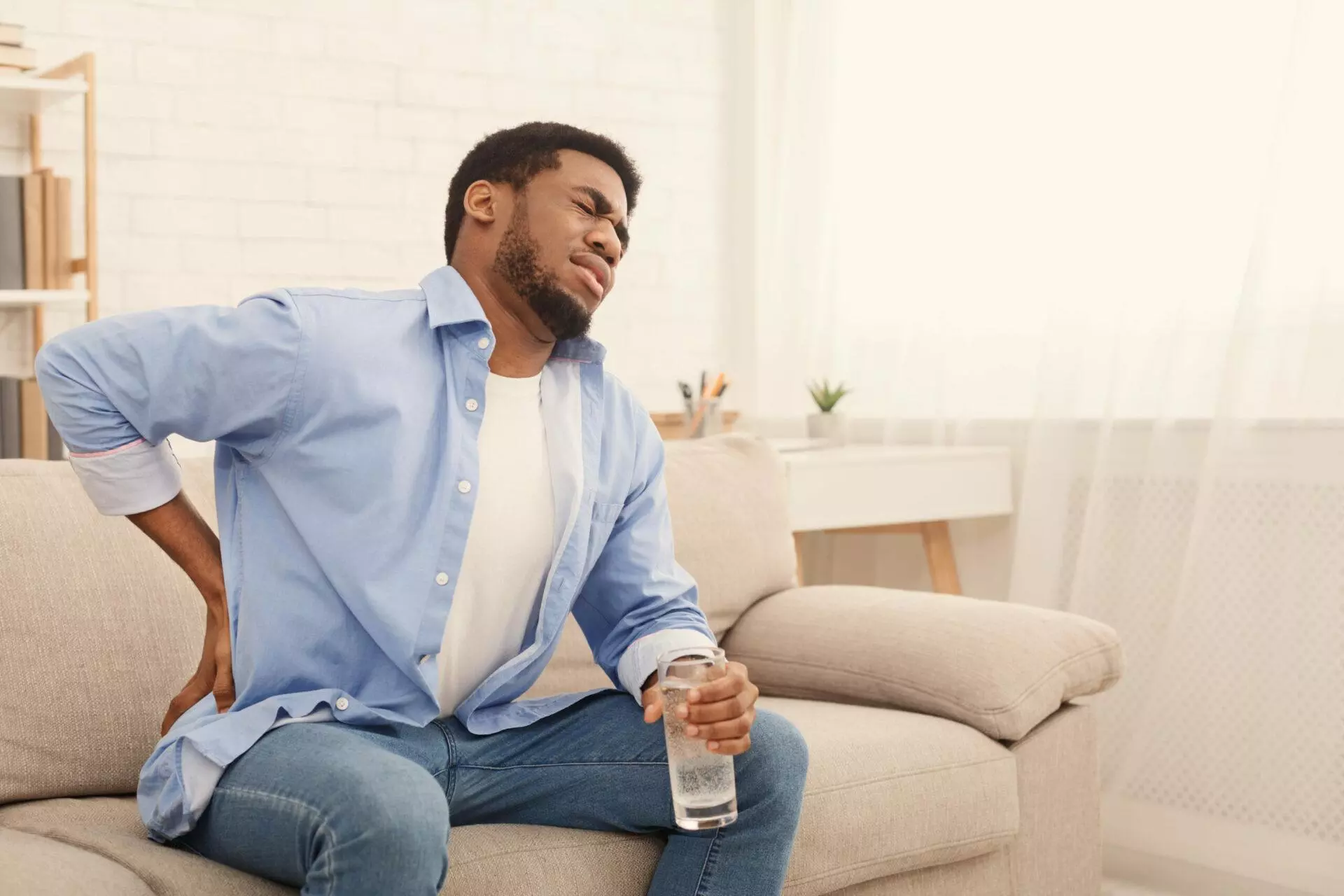 Man with back pain holding glass of water at home
