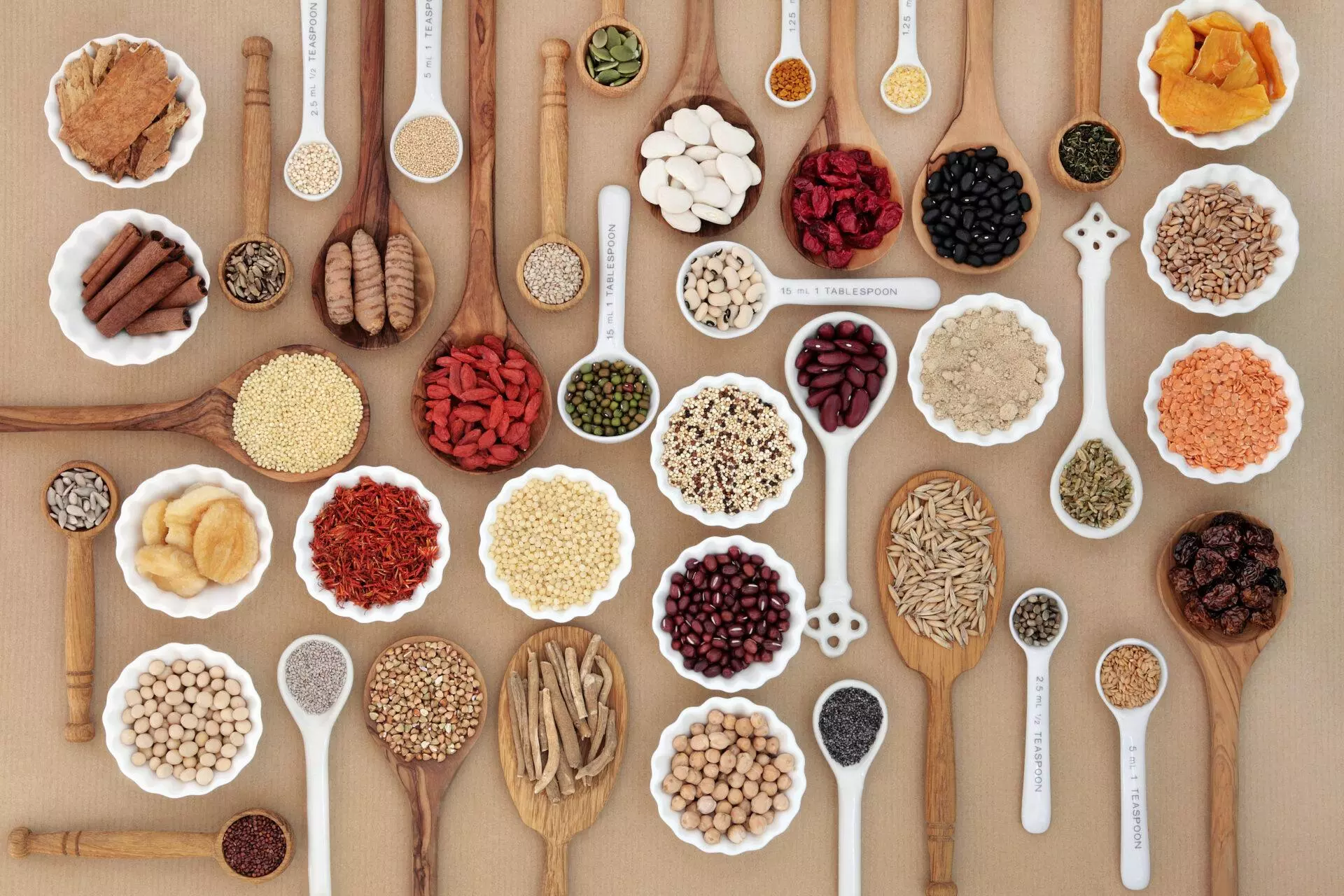 Spoons and bowls with vitamins and supplements on brown background.