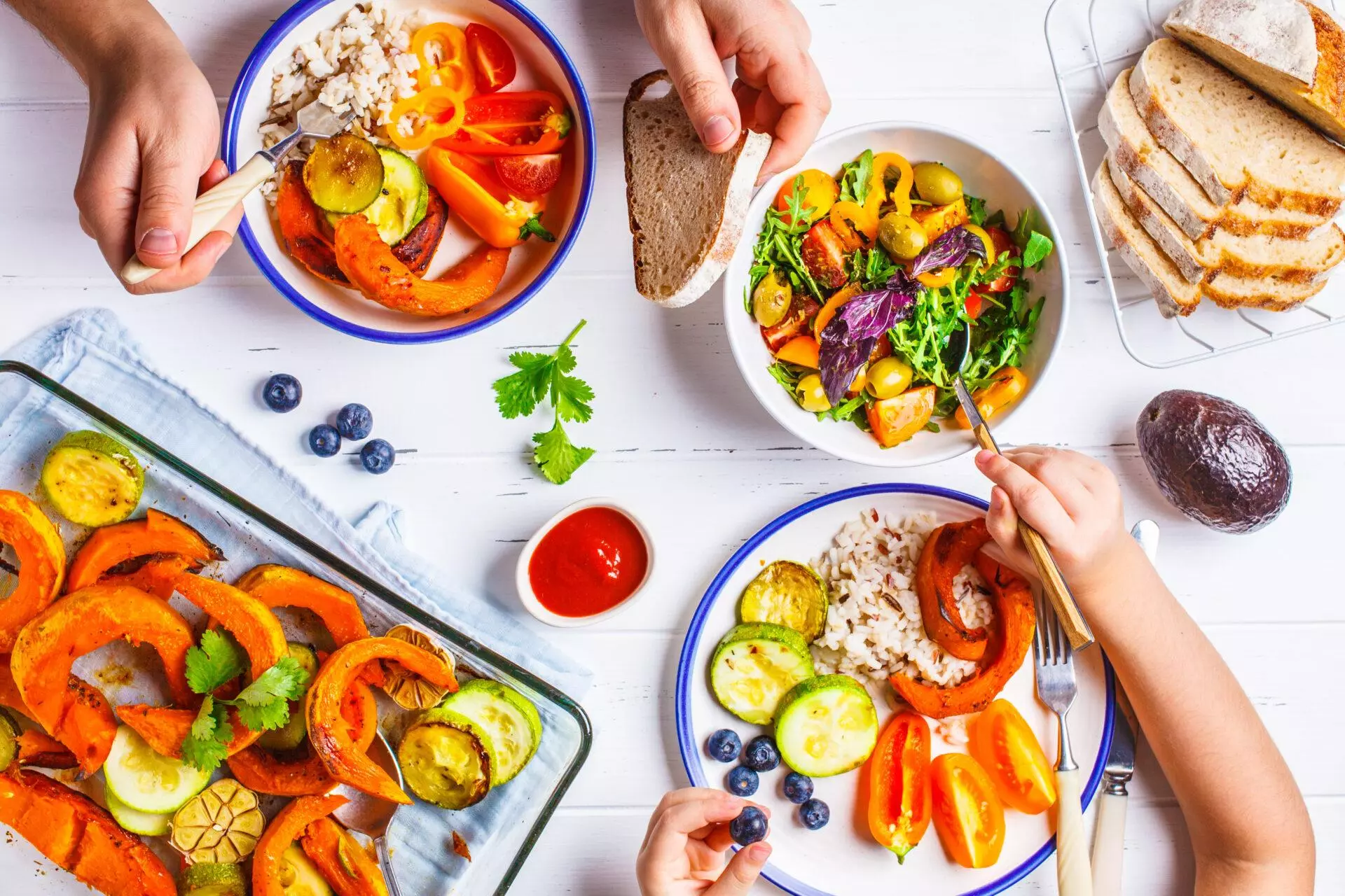 Flat lay of family hands eating healthy food. Baked vegetables, fresh salad, berries and bread on a white background.