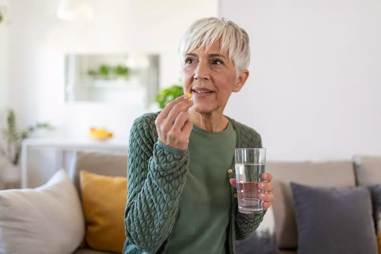 Senior woman takes a pill with a glass of water in hand.