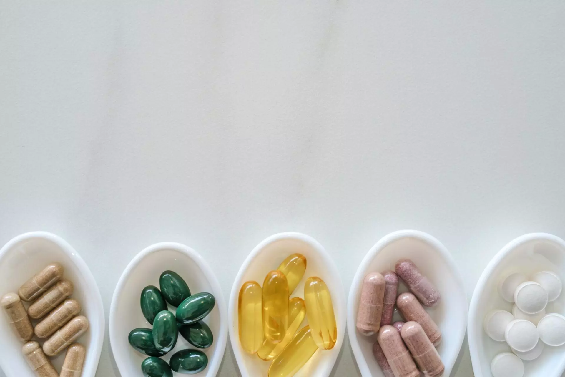 Supplements on white spoons on marble texture background.