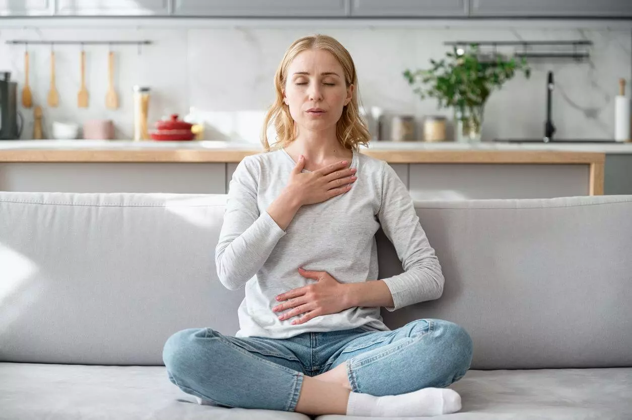 Woman sitting on a sofa doing calming breathing exercises.