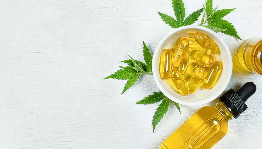 Cannabis oil, capsules and hemp leaves on a white surface