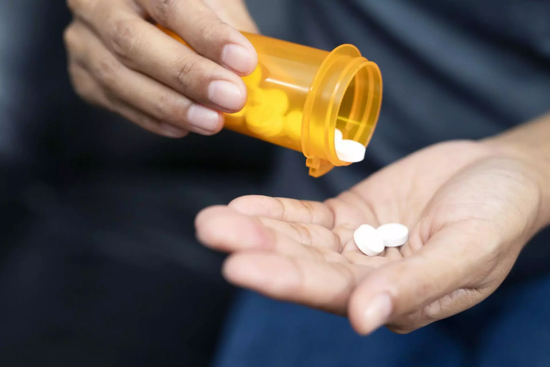 Woman hand with pills out of a bottle on dark background