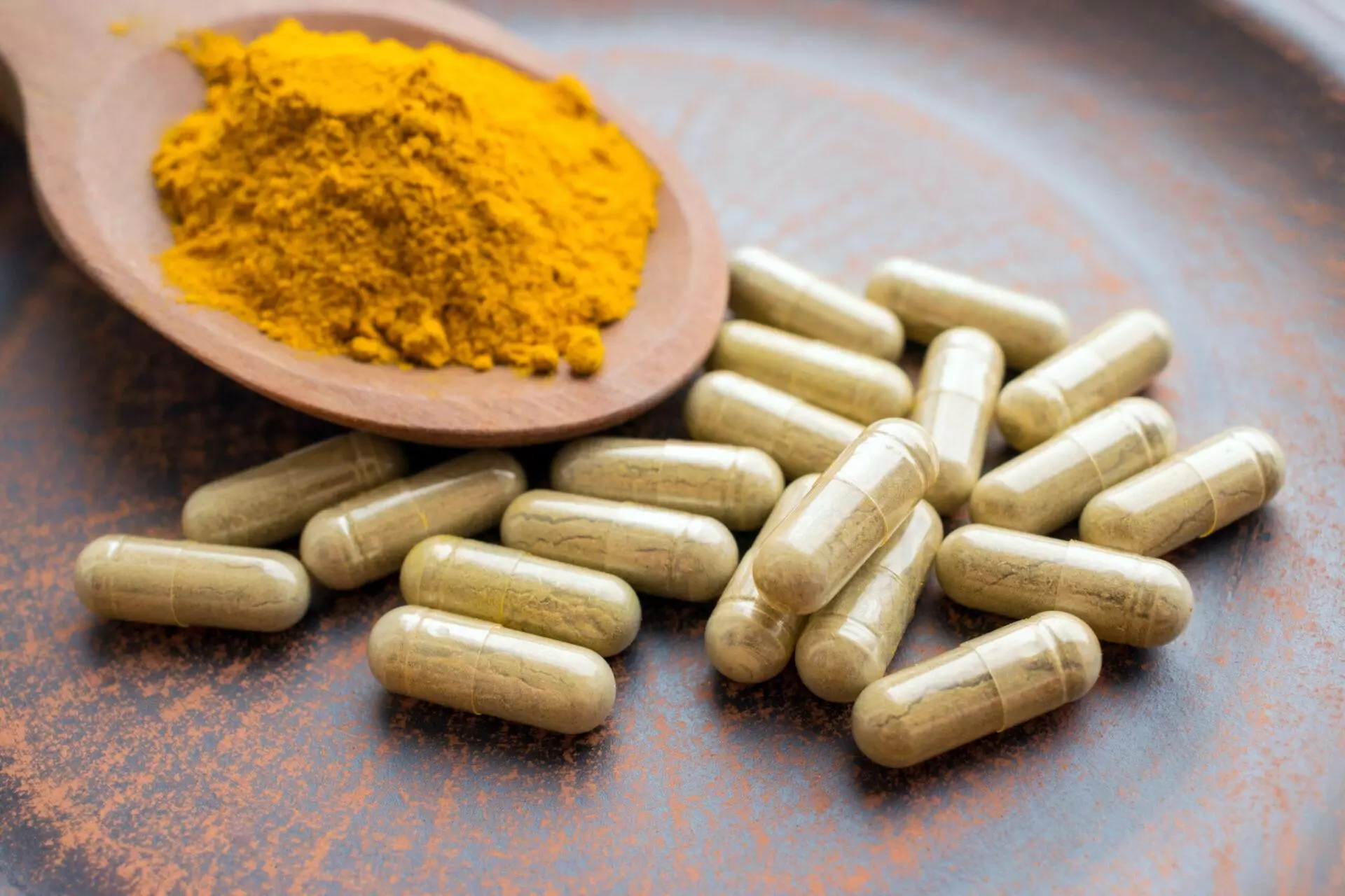 Turmeric capsules and spoon with orange curcumin powder on clay plate