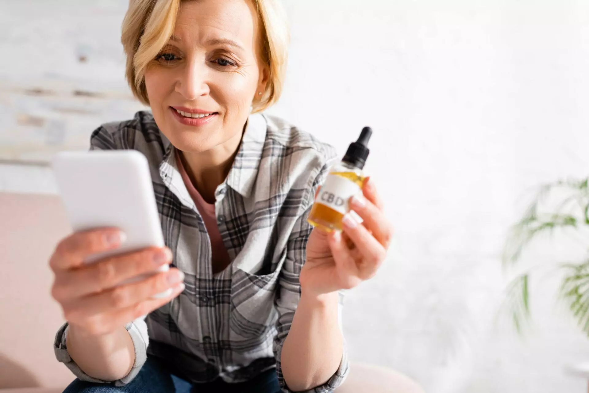 Image of a happy woman holding a bottle of CBD oil and pressing her phone. 