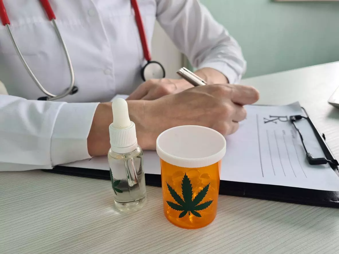 A doctor writing a prescription with a bottle of cannabis oil and a container of medical marijuana capsules on the table.