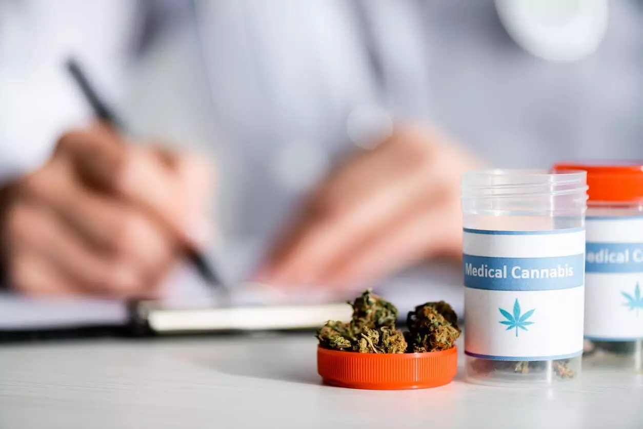 A close-up of medical cannabis containers and buds, with a doctor writing in the background.